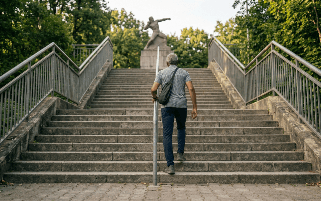 Mann Mitte 60 steigt eine lange Treppe im Park hoch, Symbol für Durchhaltevermögen und Inbewegungbleiben